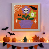 Tableau punch needle chaudron fleuri accroché au mur dans une déco d'Halloween