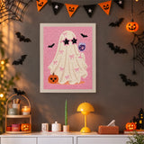 Tableau punch needle fantôme aux nœuds roses accroché au mur dans une déco d'Halloween