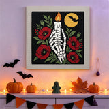 Tableau punch needle main de squelette et bougie accroché au mur dans une déco d'Halloween