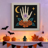 Tableau punch needle main de squelette et roses accroché au mur dans une déco d'Halloween
