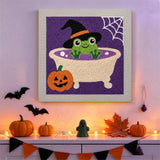 Tableau punch needle grenouille au bain accroché au mur dans une déco d'Halloween
