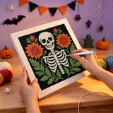 Broderie punch needle en cours, aiguille en main, sur la toile du squelette aux fleurs orange