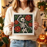 Tableau punch needle squelette dansant parmi les fleurs tenu en main pour montrer sa taille