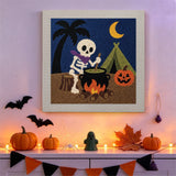Tableau punch needle squelette au feu de camp accroché au mur dans une déco d'Halloween